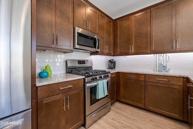 kitchen with light wood-type flooring, appliances with stainless steel finishes, backsplash, and light stone counters