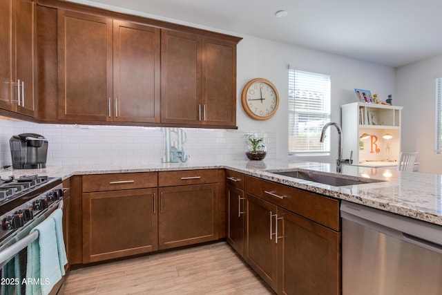 kitchen with sink, light wood-type flooring, light stone countertops, appliances with stainless steel finishes, and tasteful backsplash