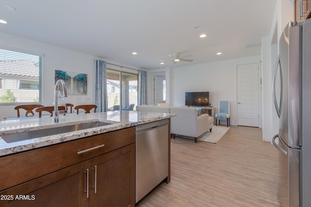 kitchen with sink, light hardwood / wood-style flooring, ceiling fan, appliances with stainless steel finishes, and light stone counters