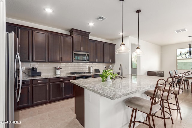 kitchen featuring light stone counters, pendant lighting, a center island with sink, and stainless steel appliances