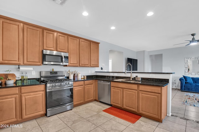 kitchen with kitchen peninsula, dark stone countertops, sink, light tile patterned flooring, and appliances with stainless steel finishes