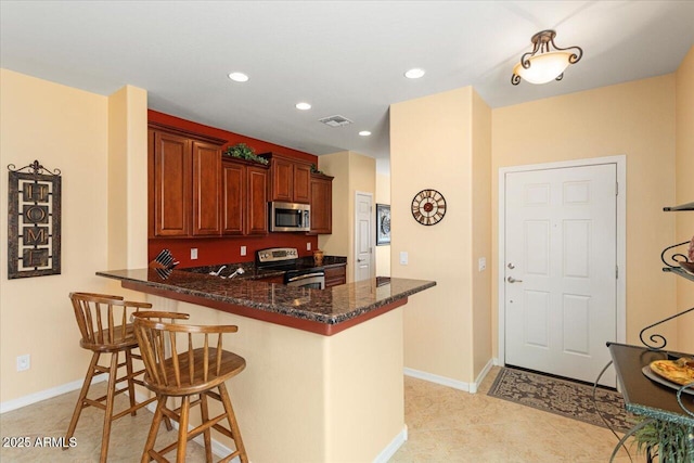 kitchen featuring stainless steel appliances, a breakfast bar, a peninsula, visible vents, and dark stone countertops