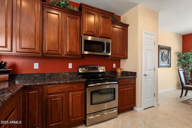 kitchen with baseboards, stainless steel appliances, dark stone countertops, and light tile patterned flooring