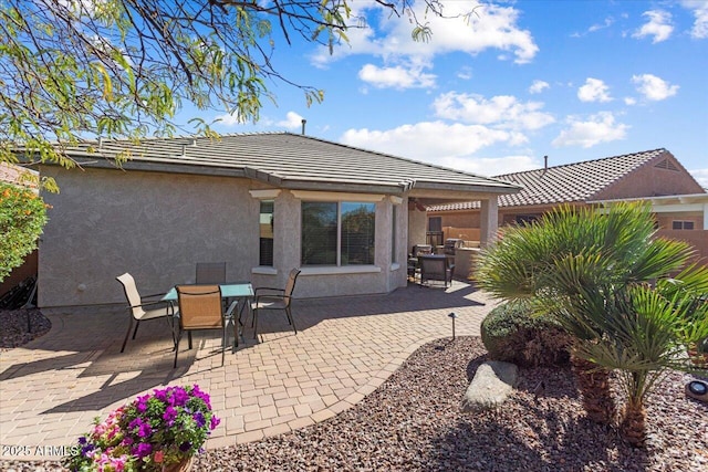 rear view of property with outdoor dining area, a patio area, a tile roof, and stucco siding