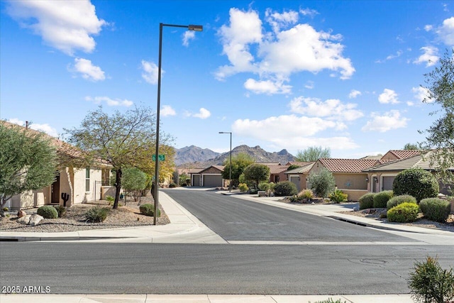 view of road featuring sidewalks, a mountain view, curbs, a residential view, and street lighting