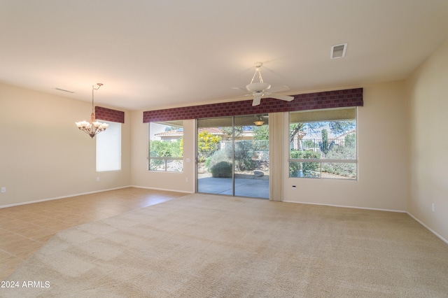 carpeted spare room with a healthy amount of sunlight and ceiling fan with notable chandelier