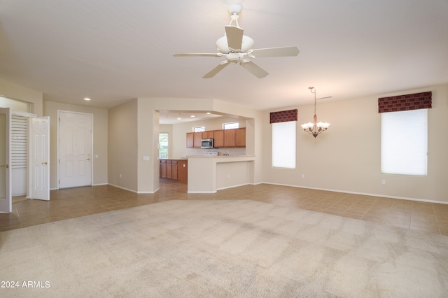 unfurnished living room with ceiling fan with notable chandelier and light carpet