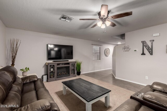 living area with ceiling fan, wood finished floors, baseboards, and a glass covered fireplace