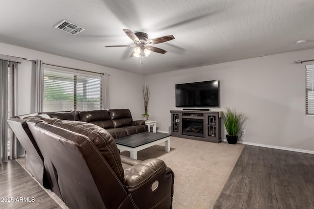 living room featuring ceiling fan, wood finished floors, baseboards, and a glass covered fireplace