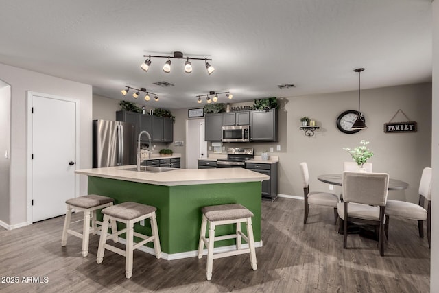 kitchen featuring stainless steel appliances, a sink, a center island with sink, dark wood-style flooring, and a kitchen bar