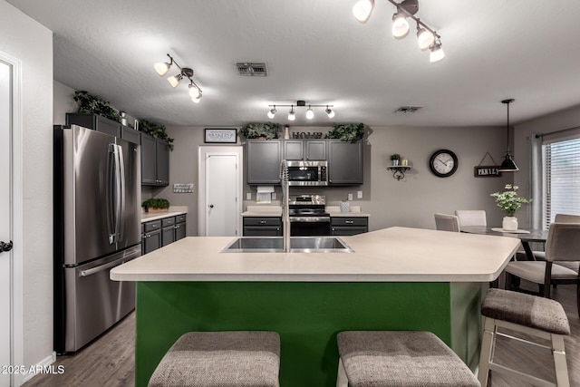 kitchen with appliances with stainless steel finishes, a sink, a breakfast bar area, wood finished floors, and light countertops