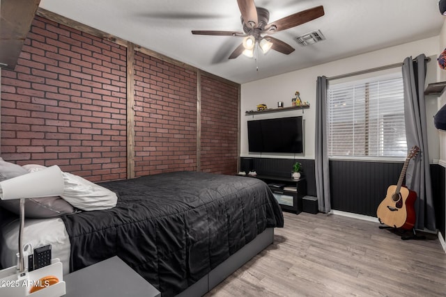 bedroom featuring brick wall, wood finished floors, wainscoting, and ceiling fan