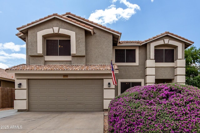 mediterranean / spanish-style home featuring stucco siding, an attached garage, a tile roof, and concrete driveway
