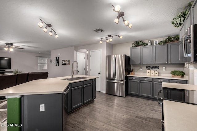 kitchen featuring stainless steel appliances, a sink, arched walkways, light countertops, and dark wood-type flooring