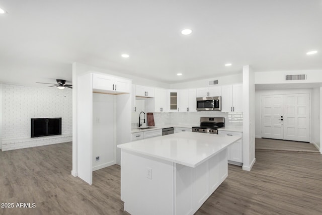 kitchen with a fireplace, a center island, white cabinets, and appliances with stainless steel finishes