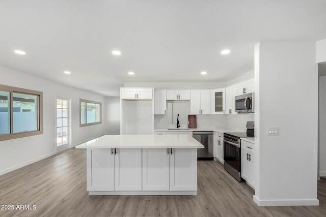 kitchen featuring appliances with stainless steel finishes, sink, white cabinets, a center island, and light hardwood / wood-style flooring