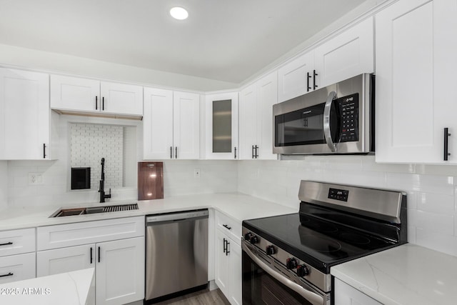 kitchen with light stone countertops, white cabinetry, appliances with stainless steel finishes, and sink