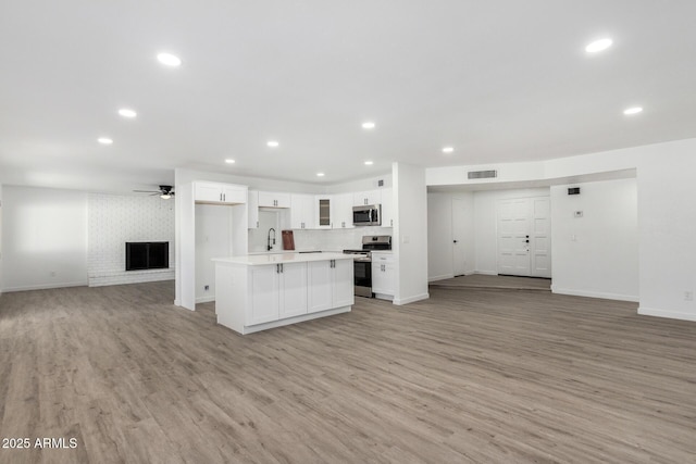 kitchen with a brick fireplace, appliances with stainless steel finishes, a kitchen island, ceiling fan, and white cabinets