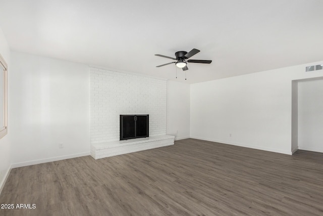 unfurnished living room featuring a brick fireplace, dark hardwood / wood-style floors, and ceiling fan