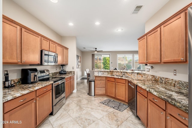 kitchen with kitchen peninsula, appliances with stainless steel finishes, light stone counters, ceiling fan, and sink