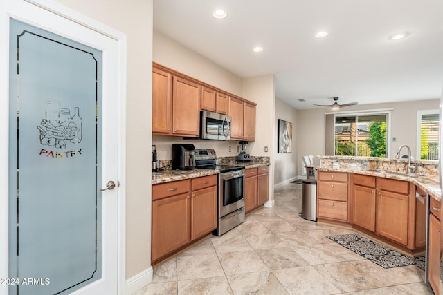 kitchen featuring light stone countertops, stainless steel appliances, ceiling fan, and sink