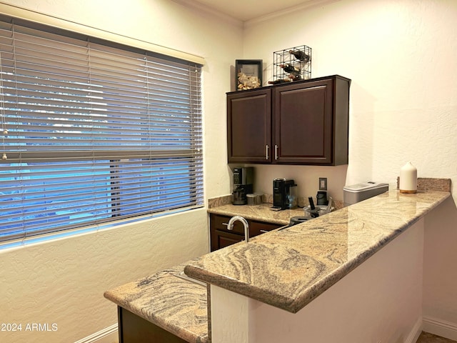 kitchen with kitchen peninsula, dark brown cabinetry, light stone counters, and ornamental molding