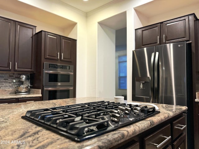 kitchen featuring dark brown cabinets, crown molding, light stone countertops, and stainless steel appliances