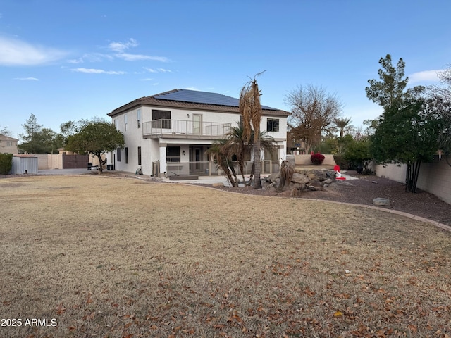 rear view of house featuring a lawn, a patio area, a balcony, and solar panels