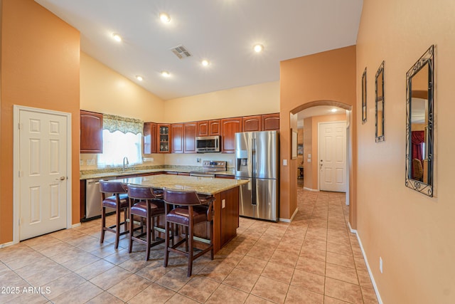 kitchen with arched walkways, visible vents, a center island, stainless steel appliances, and a sink
