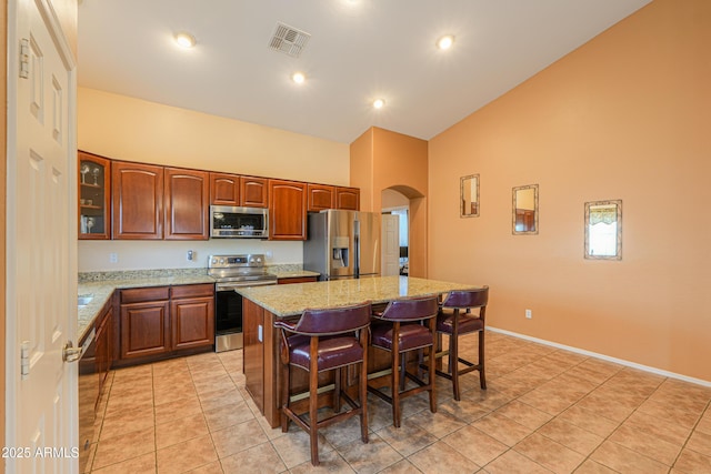 kitchen featuring arched walkways, a breakfast bar, stainless steel appliances, visible vents, and a kitchen island