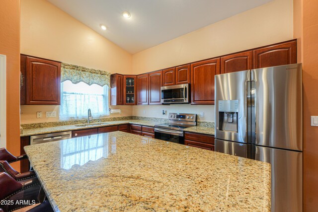 kitchen featuring light stone counters, a sink, vaulted ceiling, appliances with stainless steel finishes, and glass insert cabinets