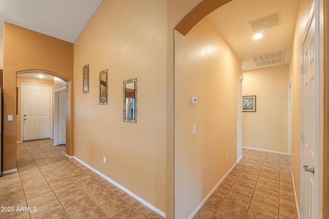 hall with arched walkways, visible vents, baseboards, and light tile patterned floors