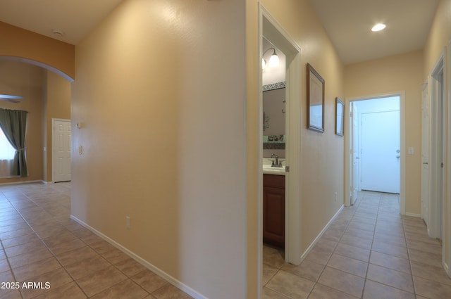 corridor featuring arched walkways, a sink, baseboards, and light tile patterned floors