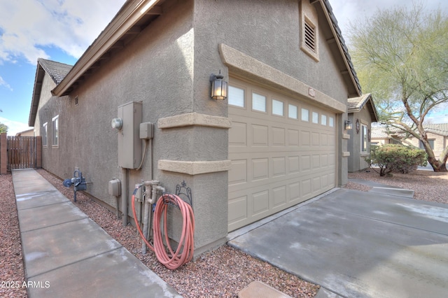 view of side of property featuring driveway, fence, and stucco siding