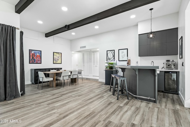 kitchen featuring decorative light fixtures, light hardwood / wood-style floors, beam ceiling, a kitchen bar, and a towering ceiling