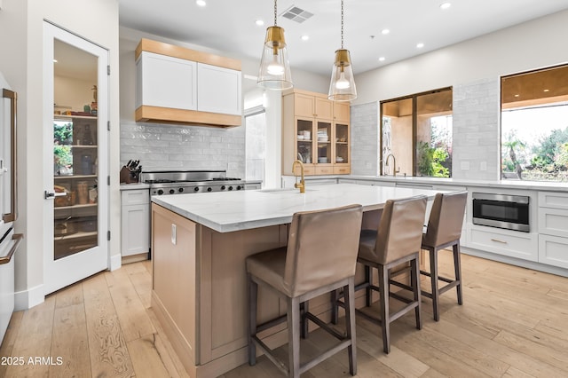 kitchen featuring sink, white cabinets, tasteful backsplash, and an island with sink