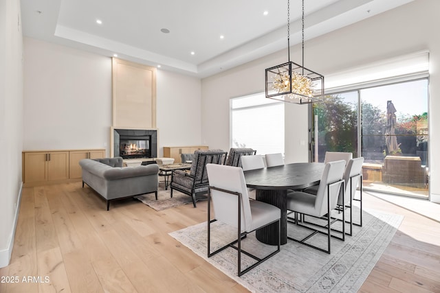 dining space with light wood-type flooring, a large fireplace, a tray ceiling, and a notable chandelier