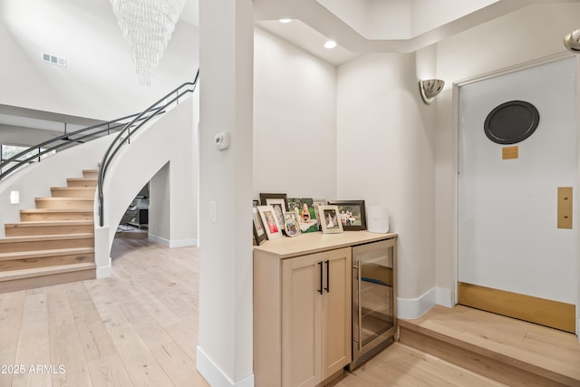 corridor with light hardwood / wood-style floors, beverage cooler, and a chandelier