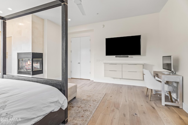 bedroom with ceiling fan, a multi sided fireplace, and light hardwood / wood-style flooring