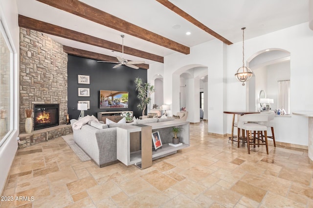 living room featuring beamed ceiling, ceiling fan, and a stone fireplace