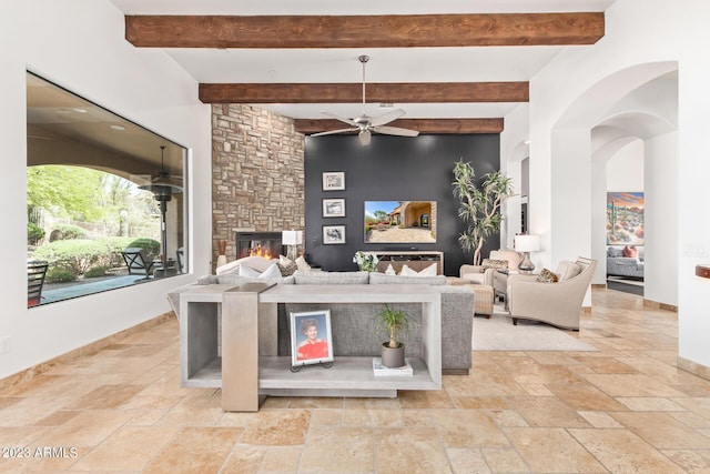 living room featuring beamed ceiling, a stone fireplace, and ceiling fan