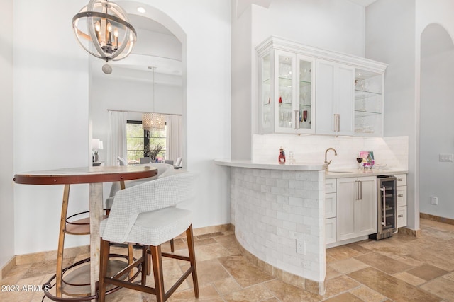 bar with wine cooler, decorative backsplash, decorative light fixtures, white cabinetry, and a chandelier