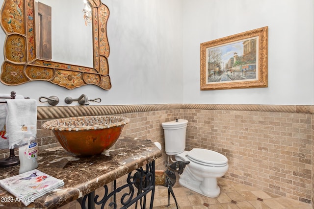 bathroom featuring sink, toilet, and brick wall