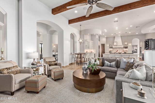 living room featuring beamed ceiling and ceiling fan with notable chandelier