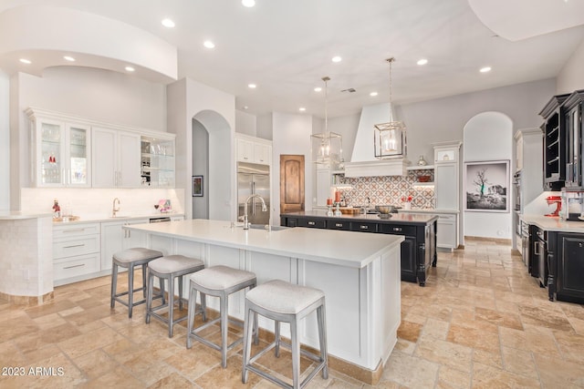 kitchen featuring white cabinetry, sink, premium range hood, decorative light fixtures, and a kitchen island with sink