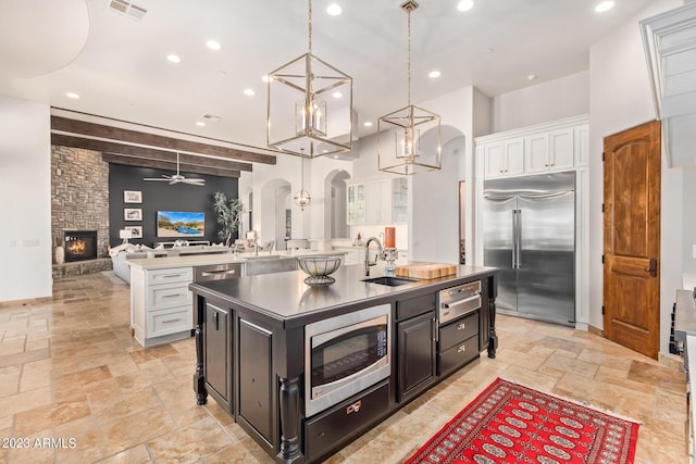 kitchen with white cabinetry, sink, hanging light fixtures, built in appliances, and a kitchen island with sink