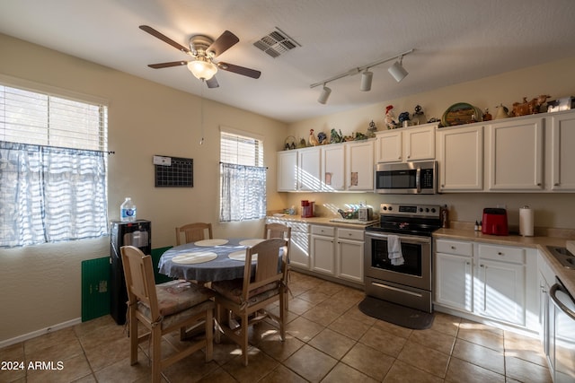 kitchen with white cabinets, rail lighting, ceiling fan, light tile patterned floors, and appliances with stainless steel finishes