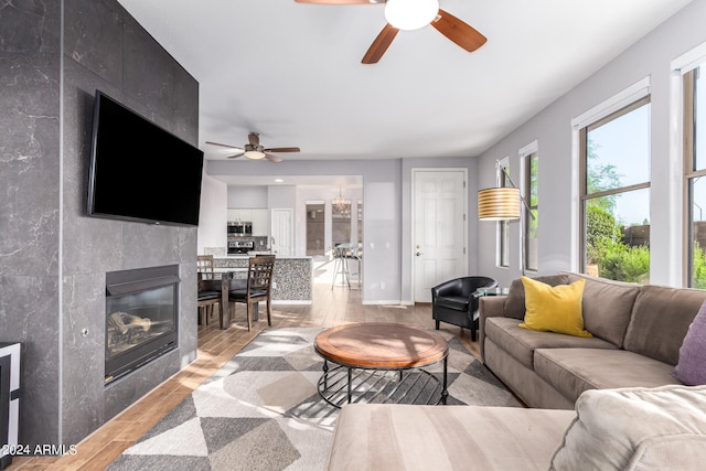 living room featuring ceiling fan, light wood-type flooring, and a fireplace