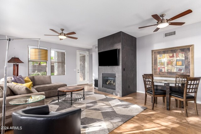 living room featuring light wood-type flooring, ceiling fan, and a large fireplace