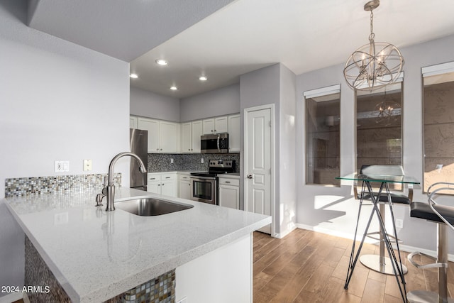 kitchen with pendant lighting, a notable chandelier, white cabinetry, stainless steel appliances, and sink